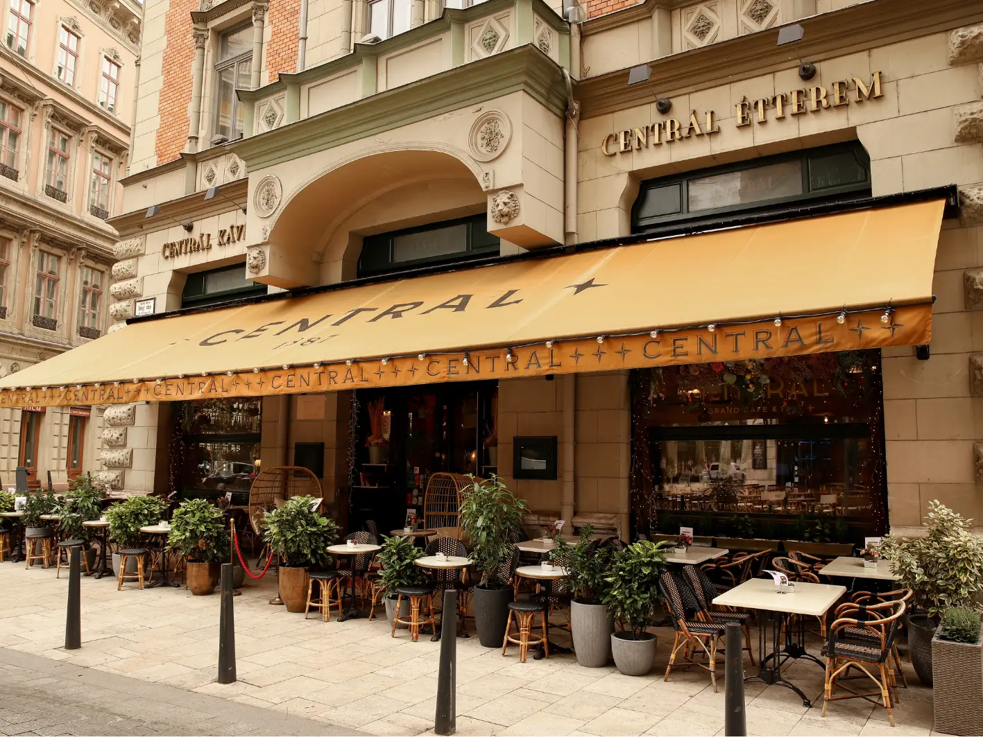 A Centrál Grand Café homlokzata a budapesti Károlyi utcában, okkersárga napellenzővel és teraszasztalokkal.