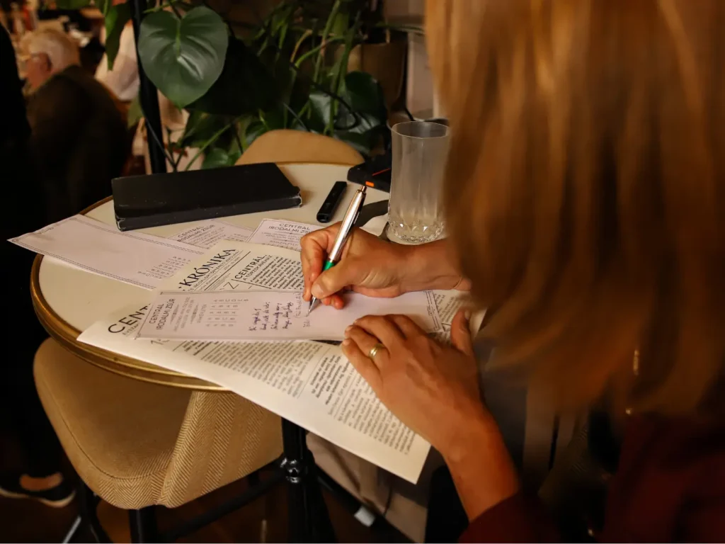 Résztvevő verset ír a Centrál Irodalmi Zsúr  irodalomóra lapjára egy kávéházi asztalnál
